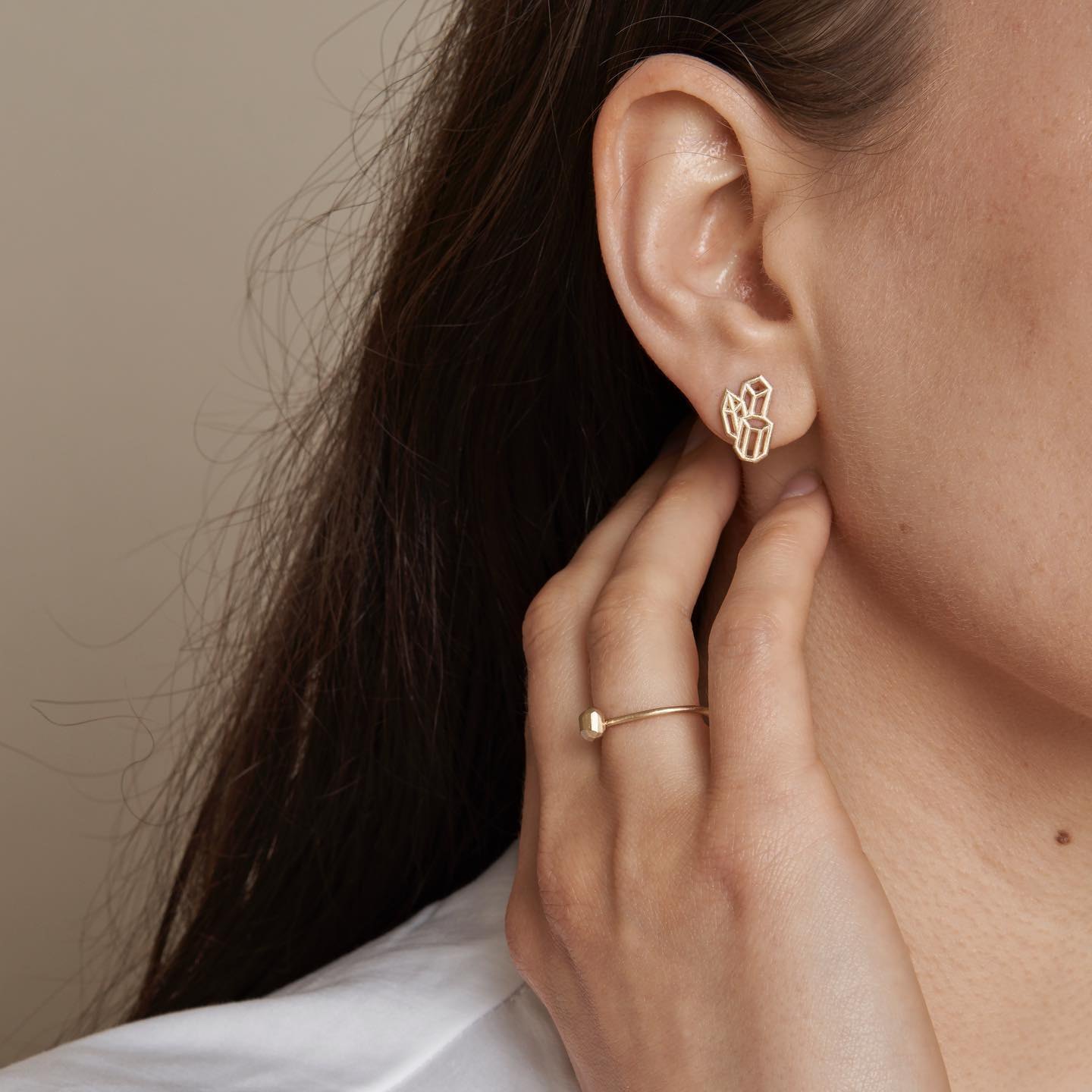 Close-up of a large geometric cluster stud earring worn with a fine ring.