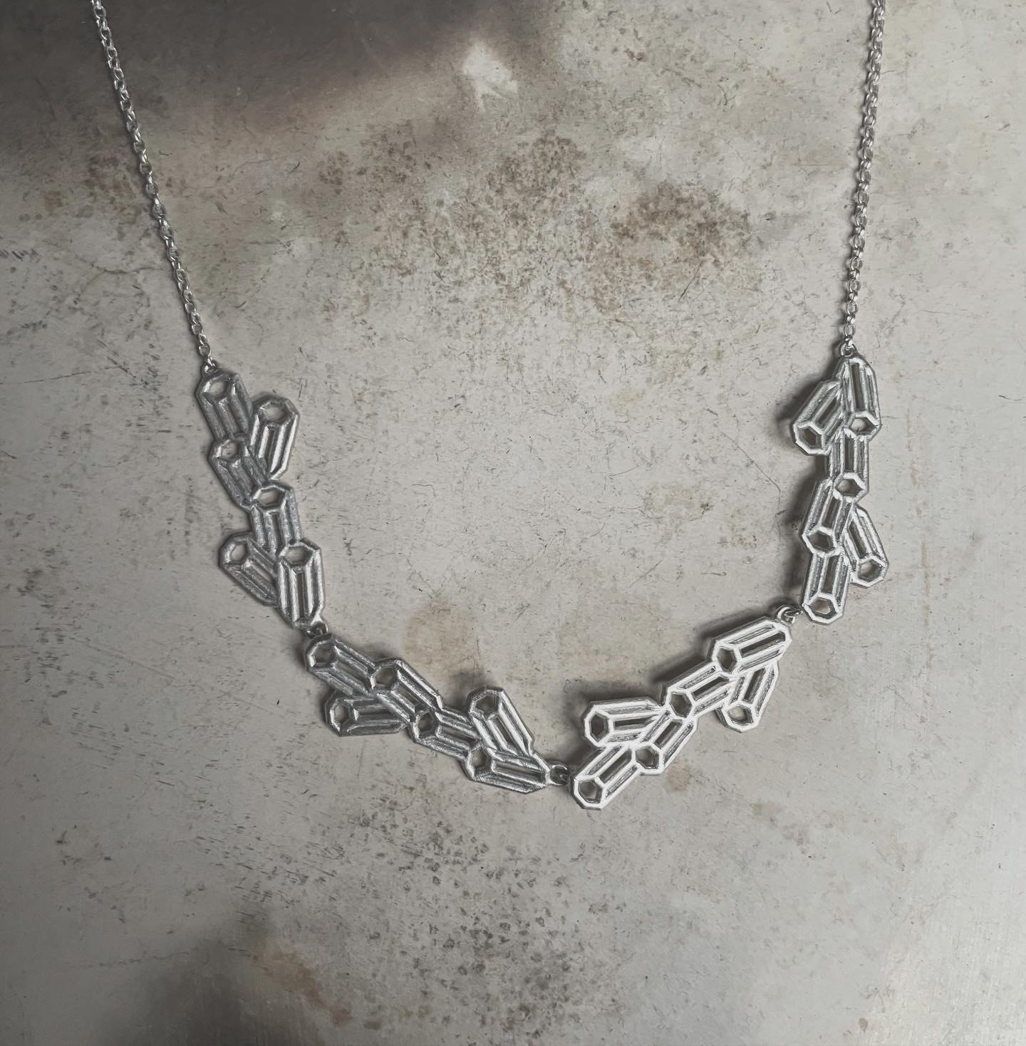 Silver geometric cluster necklace laid on a textured surface.