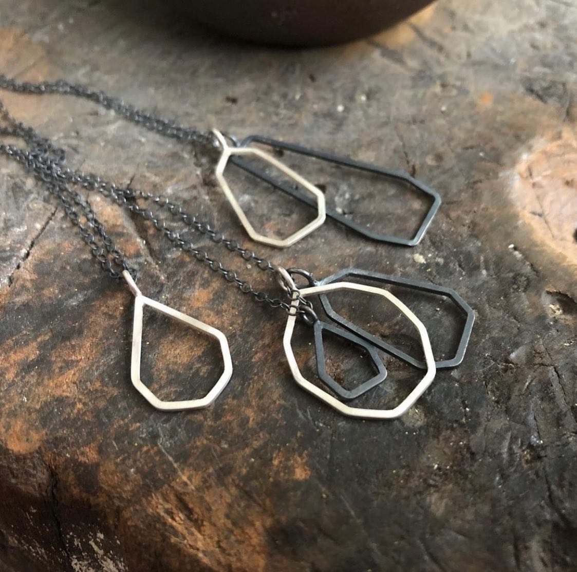 Open geometric silver and oxidised silver pendants on a jeweller's bench.