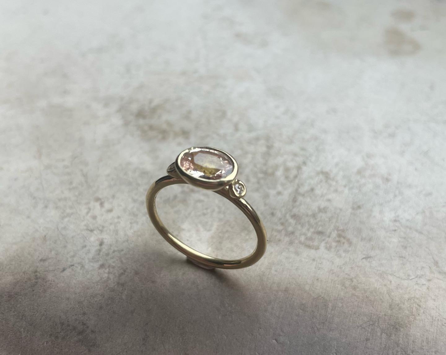 Gold ring with a pale oval stone and small accent stone.