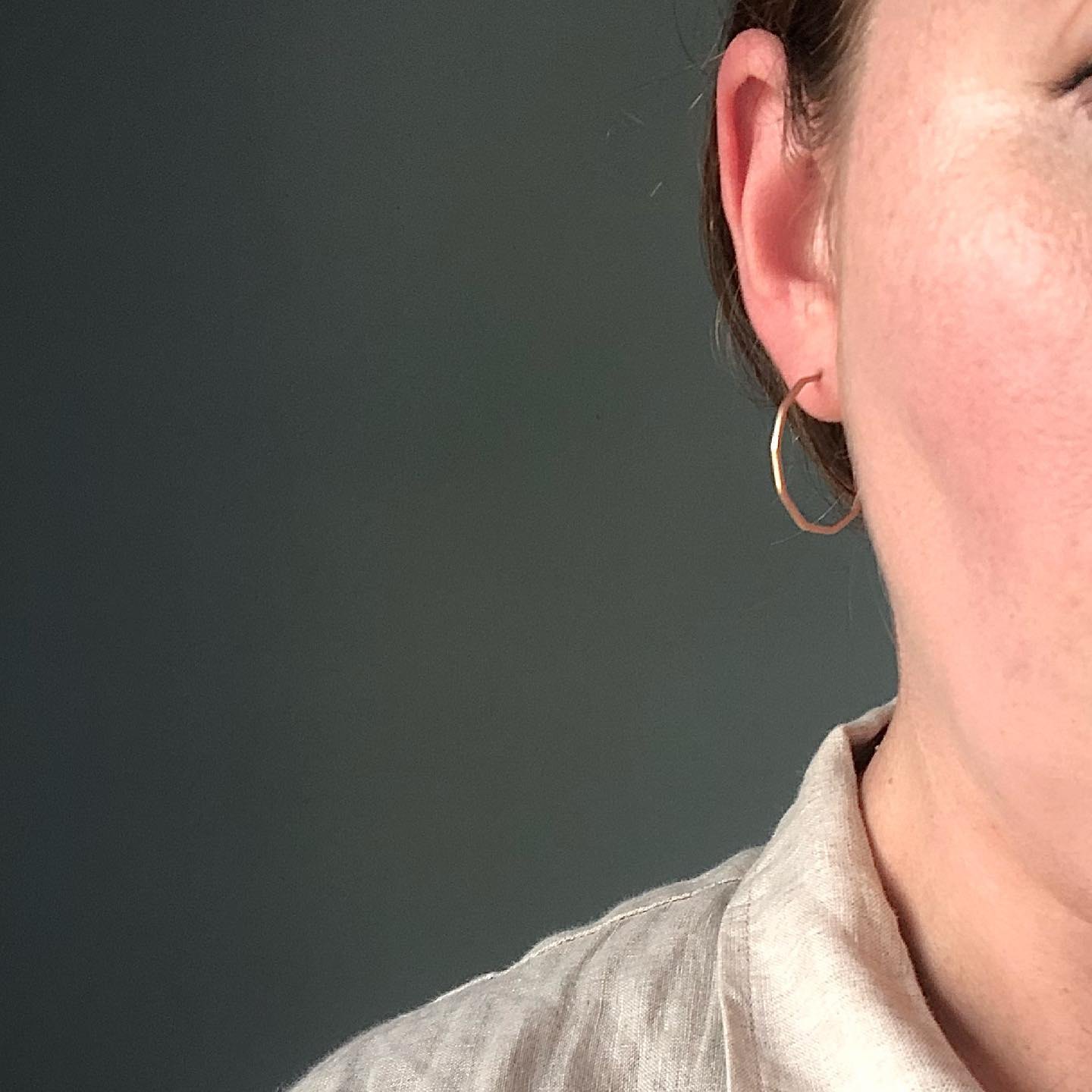 Close-up of an irregular oval hoop earring worn against a dark background.