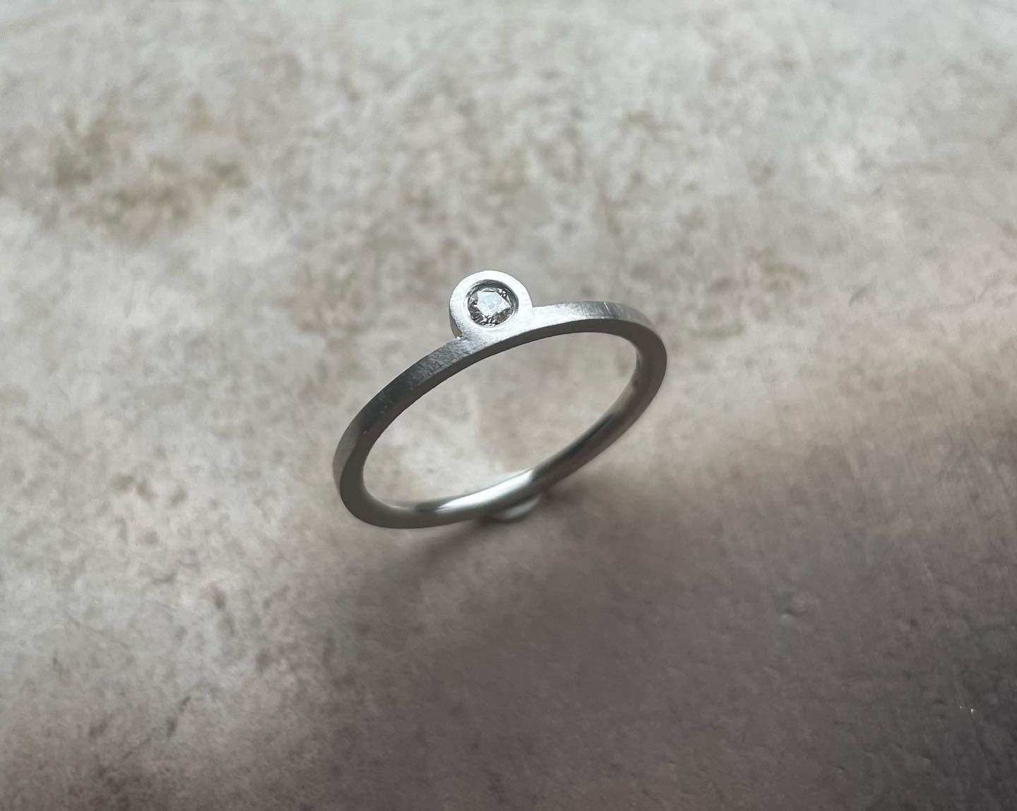 Angled view of a slim silver ring with small stone setting.