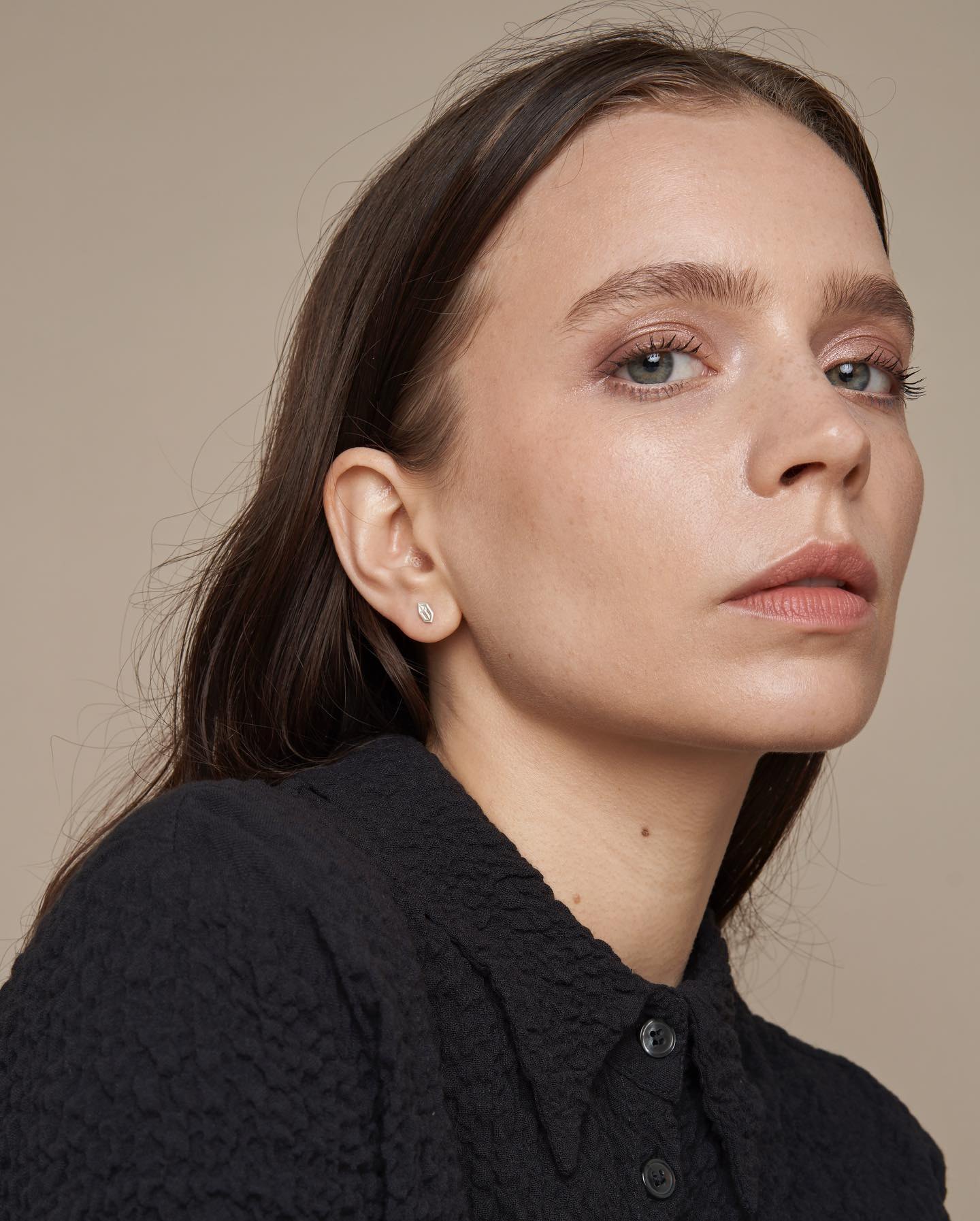 Model wearing small geometric silver stud earrings.