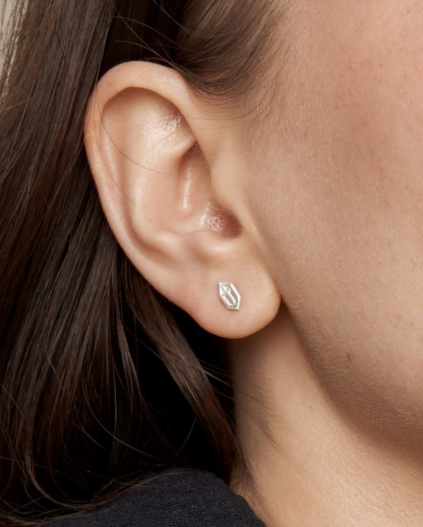 Close-up of a small geometric silver stud earring worn on the ear.