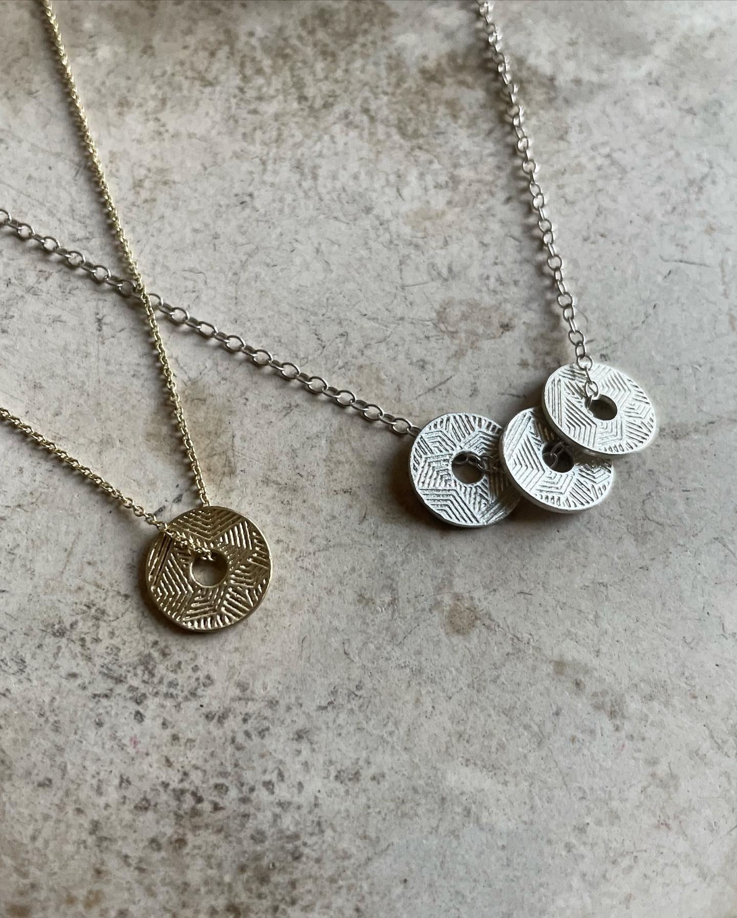 Textured circular silver and gold pendants on chains.
